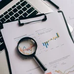 Laptop with report charts and magnifying glass on desk