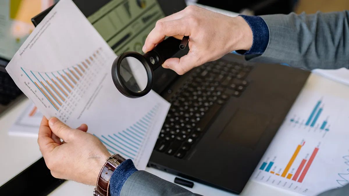 AI content writer tools with SEO features: what to look for Hands reviewing charts with magnifying glass beside laptop