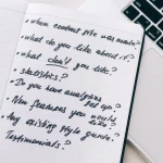 Notebook with brief questions beside a laptop